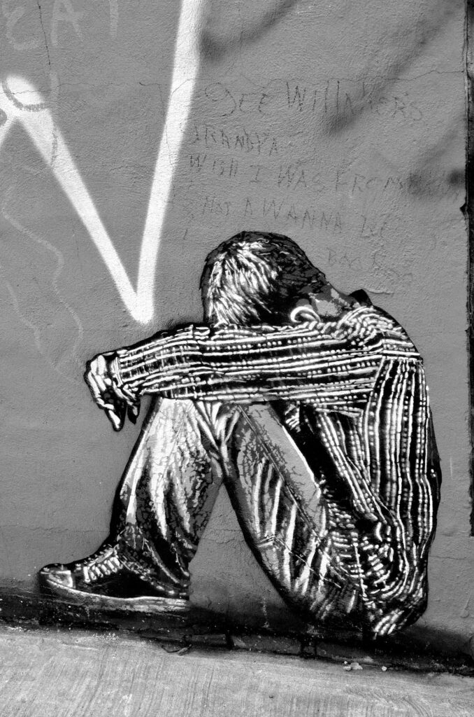 Black and white drawing of a dejected boy sitting with his head bowed between his knees, representing the wounded inner child in men.